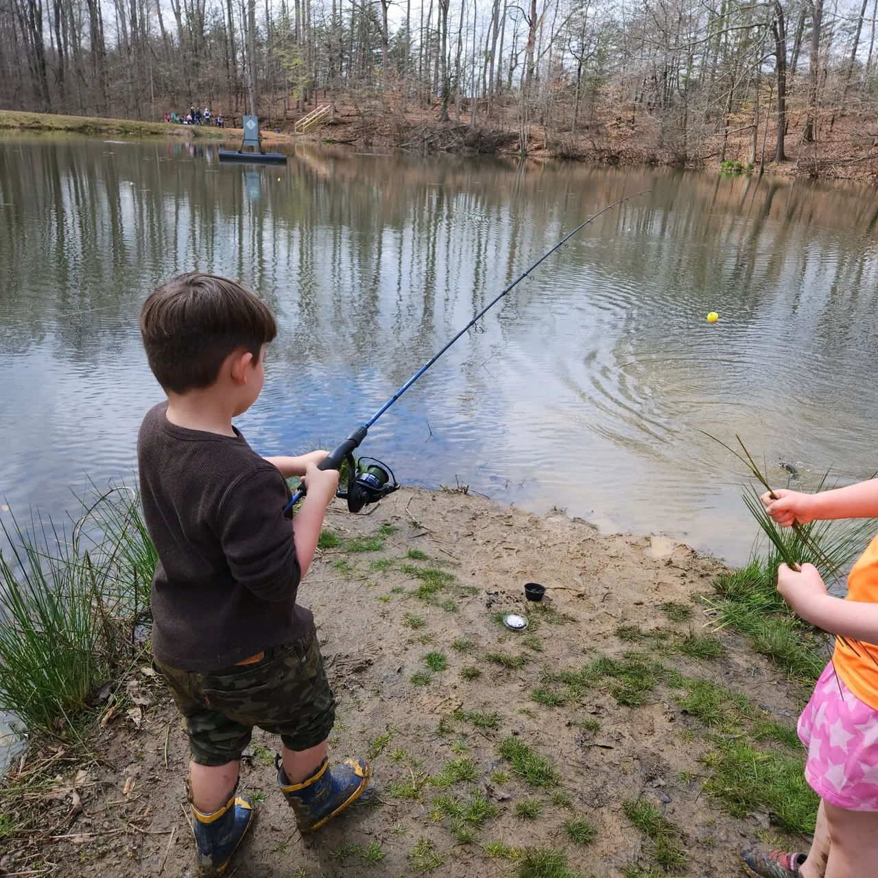Two children fishing in a pond on the shore.