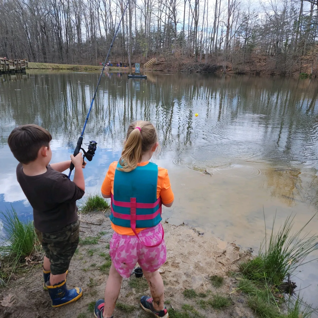 Two children fishing in a pond on a cloudy day.