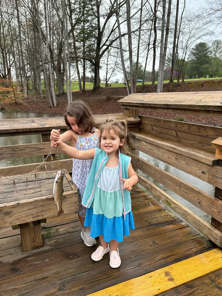 Two girls holding a fish on a wooden bridge.