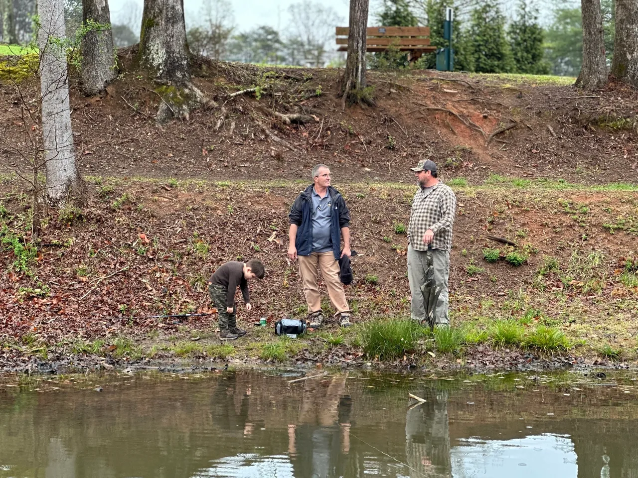 Two men fishing in a pond with another man standing next to them.