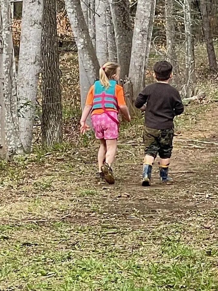 Two children are walking in the woods together.