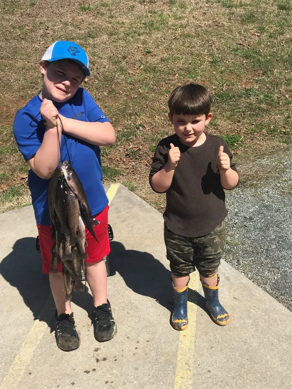 Two young boys holding fish and giving thumbs up.